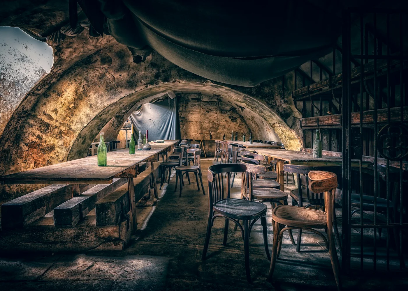 A dimly lit stone-vaulted tavern room with long wooden tables and benches